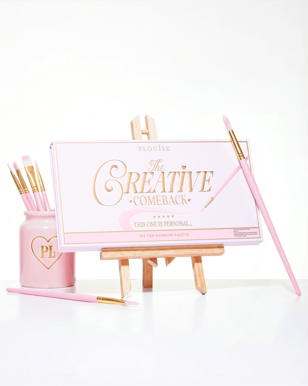 Een gesloten roze P.Louise Creative Comeback XXXL Rainbow Eyeshadow Palette geplaatst op een kunstezel omringd door make-upborstels