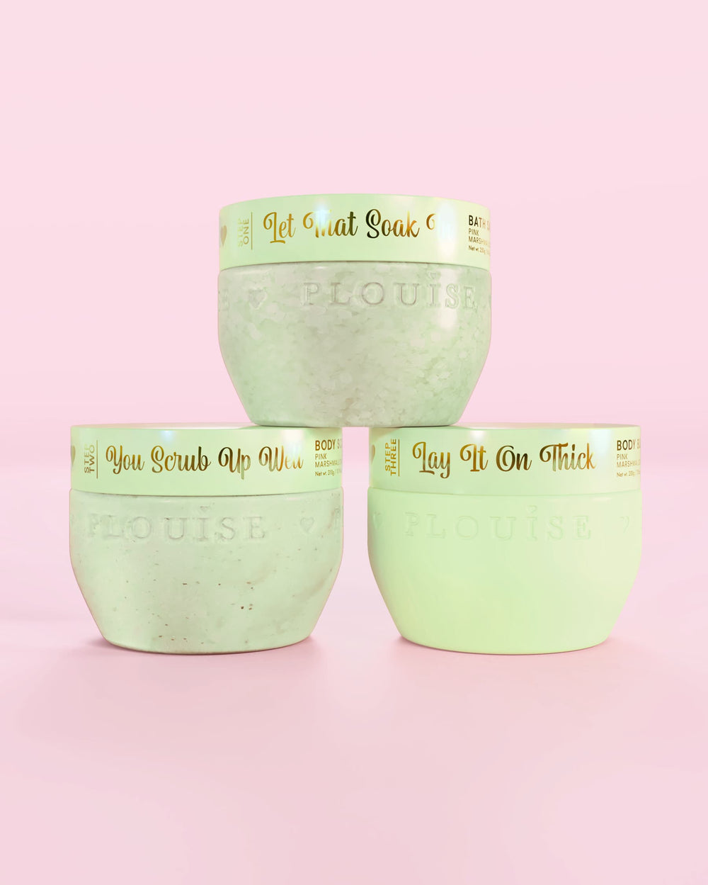 Tre P.Louise Hop Into Self-Care chokladtäckta jordgubbar gröna behållare med badsalt, kroppsskrubb och kroppssmör med guldtext på en rosa bakgrund
