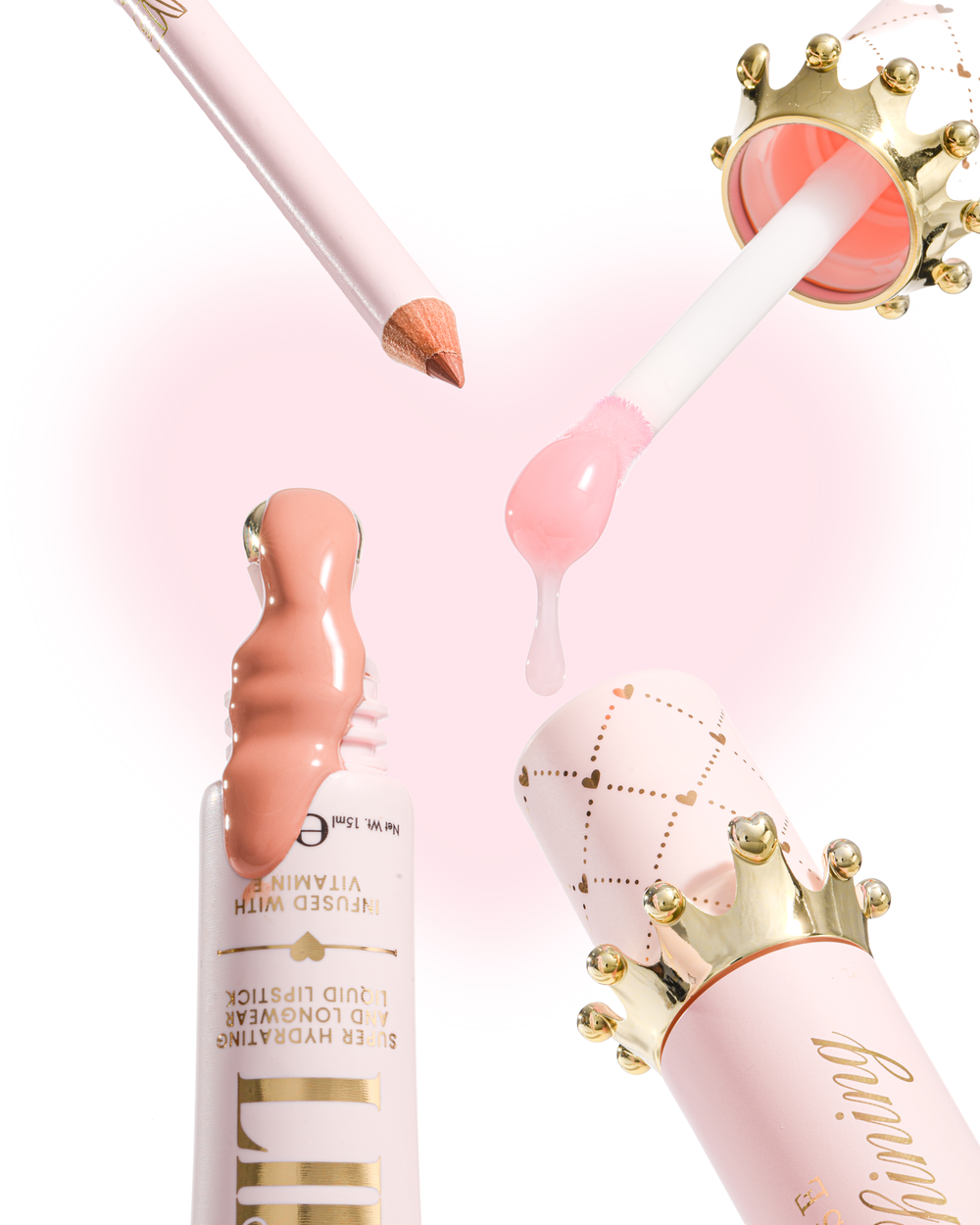 Composants de produits cosmétiques roses et dorés disposés sur un fond blanc, comprenant un tube de base pour les lèvres avec un brillant rose pêche, un applicateur pied-de-biche avec de l'huile rose, un crayon rose et un capuchon décoré d'une couronne.