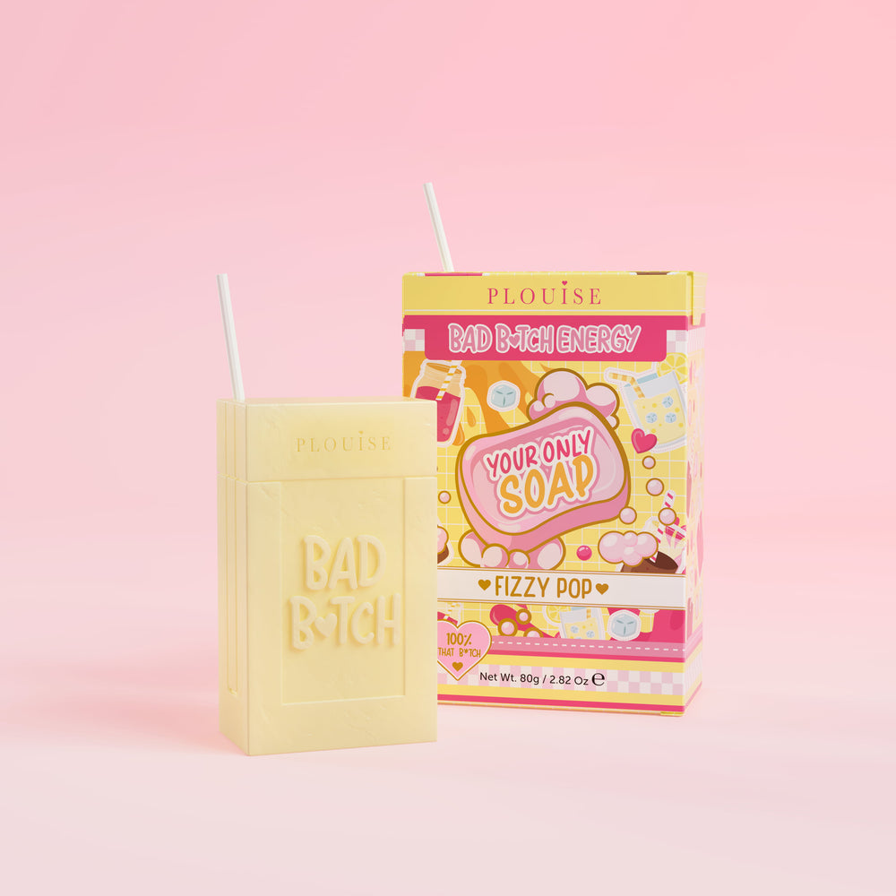 Et gult såpestykke med 'Bad Bitch' inngravert, ledsaget av en fargerik juicebokspakke med 'Fizzy Pop' merket på den, presentert på en rosa bakgrunn.