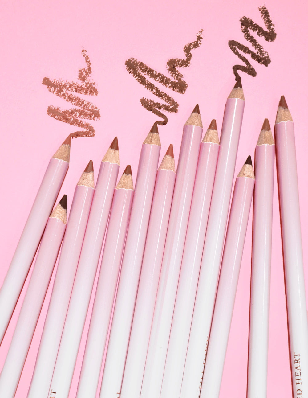 Une image de plusieurs crayons à lèvres aiguisables P.Louise Ultimate Definition regroupés montrant un produit dessiné au-dessus d'eux sur un fond rose.