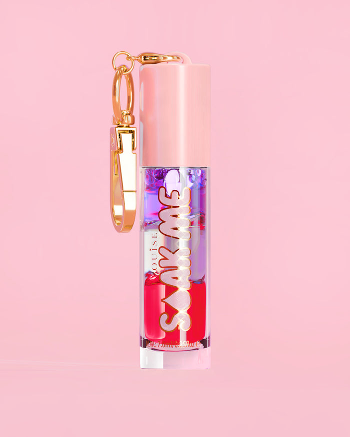 P. Louise Soak Me Lip Oil med färgglad lagerolja i en rosa tub med ett guldlås på en rosa bakgrund