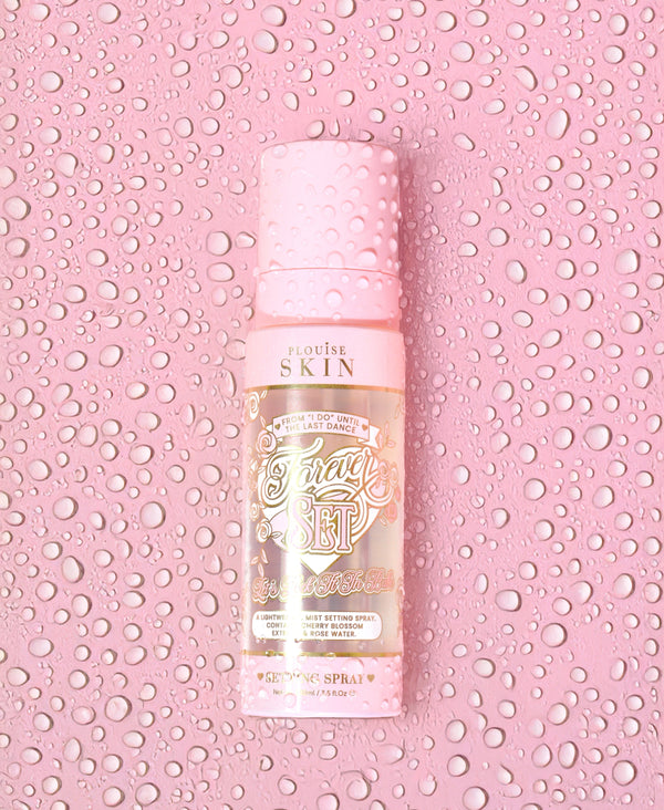 An image of the P.Louise Forever Set setting spray covered in water droplets on a pink background covered in water droplets