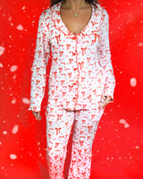 Shot van het lichaam van een vrouw, gekleed in een feestelijke set roze en wit gestreepte pyjama's met rode strikmotieven erop tegen een rode achtergrond en sneeuwvlokken