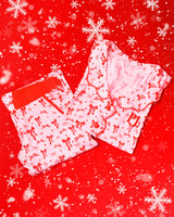 Paar roze en wit gestreepte pyjama's met rode feestelijke strikontwerpen op een rode achtergrond met sneeuwvlokken