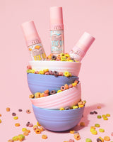 Hög med färgglada skålar fyllda med flingor som häller ut och tre flaskor med P. Louise Frosted Fix Uo Blurring Setting Spray i den översta skålen på en rosa bakgrund