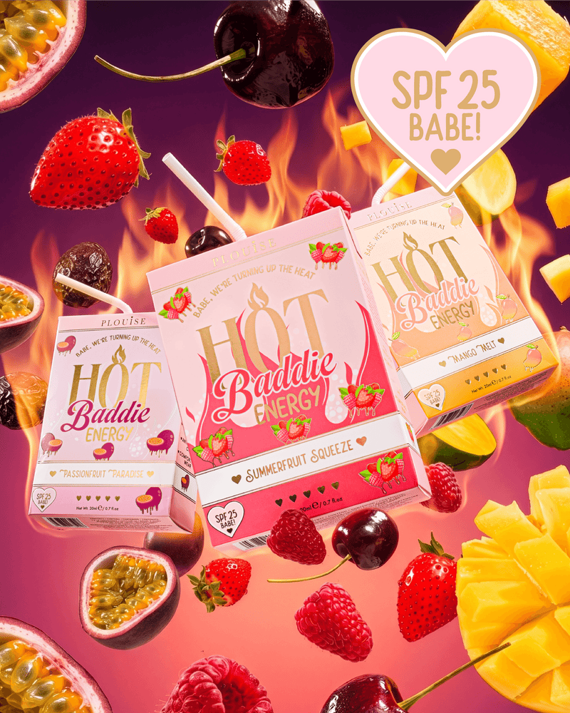 Three juice boxes from Hot Baddie Energy SPF Lip Conditioner and Lip Oil Duo are arranged in a dynamic floating composition surrounded by fresh fruit slices, cherries, strawberries, and passion fruit on a vibrant pink and orange background with flame graphics. 