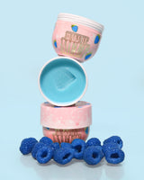 3 potjes P. Louise Make It Melt Makeup Removal Cleansing Balm in blauwe framboos op elkaar met de middelste open met blauwe crème omringd door blauwe frambozen op een blauwe achtergrond