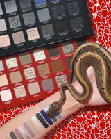 P.Louise Mystic Moonlight halloween oogschaduw & make-up palet met swatches op een arm met een slang eromheen gewikkeld tegen een rode spinnenwebachtergrond
