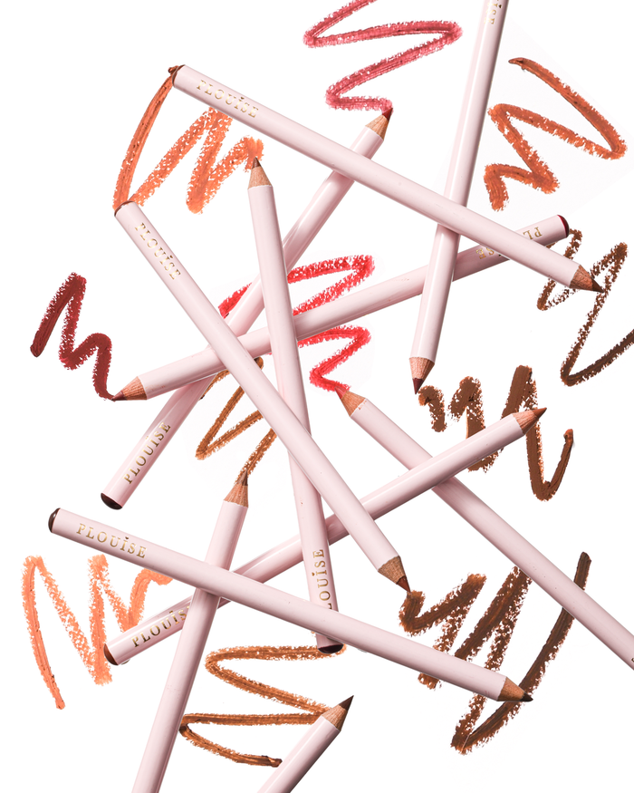 A set of pale pink P.Louise lip liner pencils arranged in a dynamic, overlapping composition on a white background, with vibrant, colourful product swatches scribbled behind them.