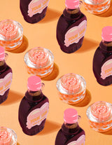 A P.Louise Dose of Dreams C-vitamin kapszula krém átlátszó tartályai narancssárga kapszulákkal, narancssárga alapon lila és rózsaszín szirupos üvegekkel körülvéve