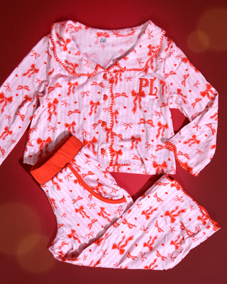 Set of pink and white striped kids christmas pyjamas with red bow designs on them against a red background