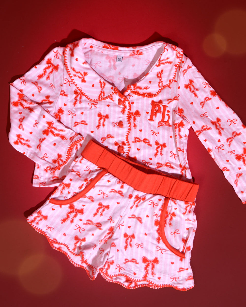 Conjunto de pijamas de Natal infantis listrados rosa e brancos com desenhos de laço vermelho sobre um fundo vermelho