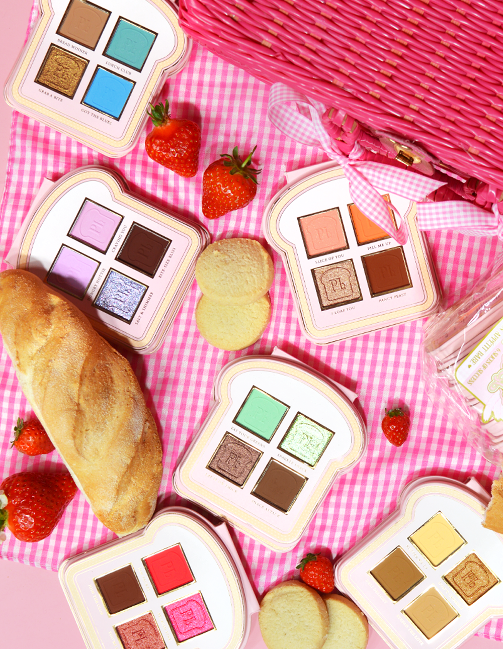 Een set mini-oogschaduwpaletten in sandwichstijl met verschillende tinten make-upkleuren op een roze gingangoppervlak, vergezeld van aardbeien en een stuk brood.