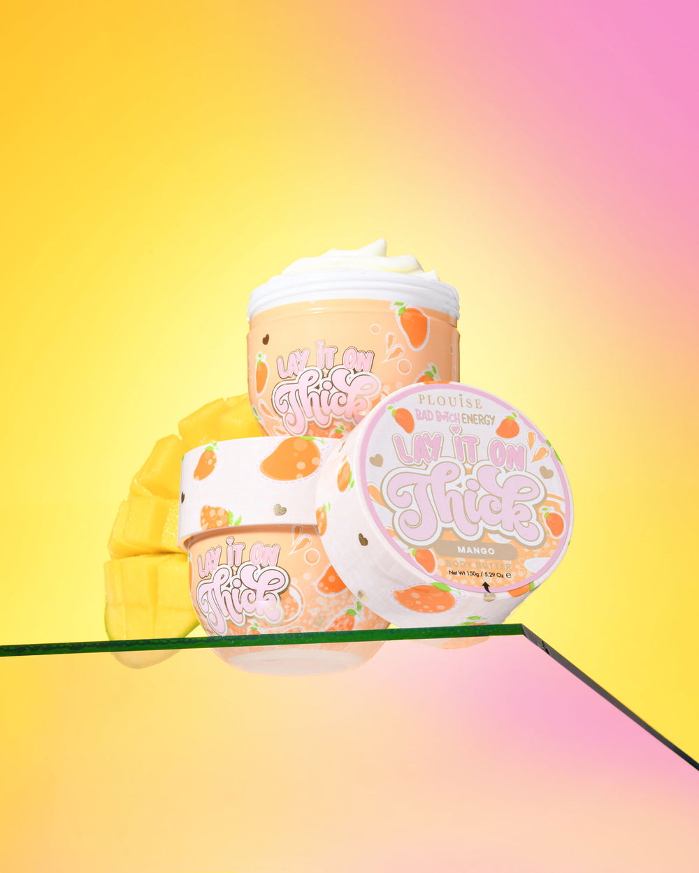 Drie containers P. Louise 'Lift It On Thick' mango body butter op een gradiënt gele en roze achtergrond