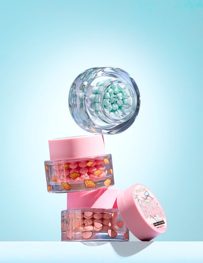 Tre små krukker med farverig c-vitamin kapsel i en gel på en lyseblå baggrund