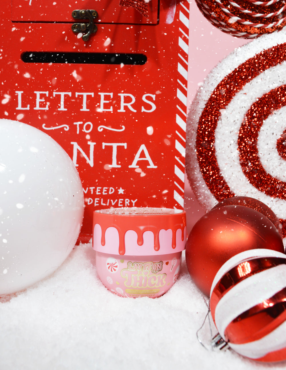 Een pot P.Louise Lay It On Thick Body Butter in Frosted Peppermint-variant, uitgestald met kerstversieringen eromheen, inclusief kerstverlichting en cadeautjes.