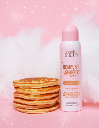 An aerosol can of P. Louise Ready Set Sparkle Glitter Setting Spray in silver Starlight Sparkle with a stack of pancakes and a pink background with sparkles