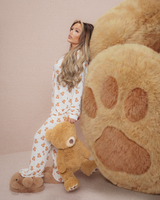 Kvinde i bamse pyjamas holder en bamse ved siden af en stor plys bjørnepote på en beige baggrund
