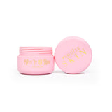 Een roze open pot P.Louise Give It A Rest Eye Cream, waarbij het deksel en de pot vanaf de zijkant zichtbaar zijn, met de merk- en productnaam op de pot in gouden letters