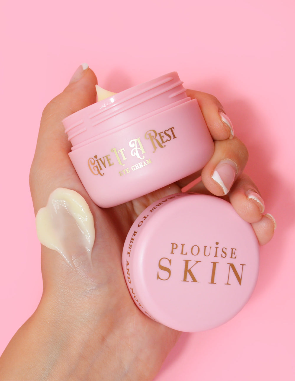 Een persoon die een roze pot P.Louise Give It A Rest oogcrème vasthoudt met de deksel eraf, met de productnaam en het merk op de pot.