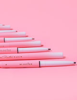 Una colección de mini lápices de cejas P.Louise colocados en fila con el nombre de la marca visible en el cuerpo de los lápices, sobre un fondo rosa.